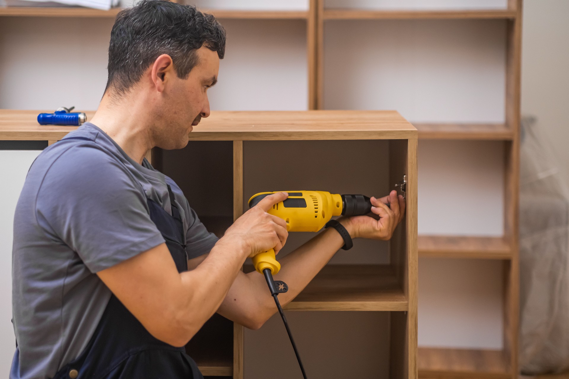 Custom furniture production focused handyman attaching door fastener to wooden cabinet